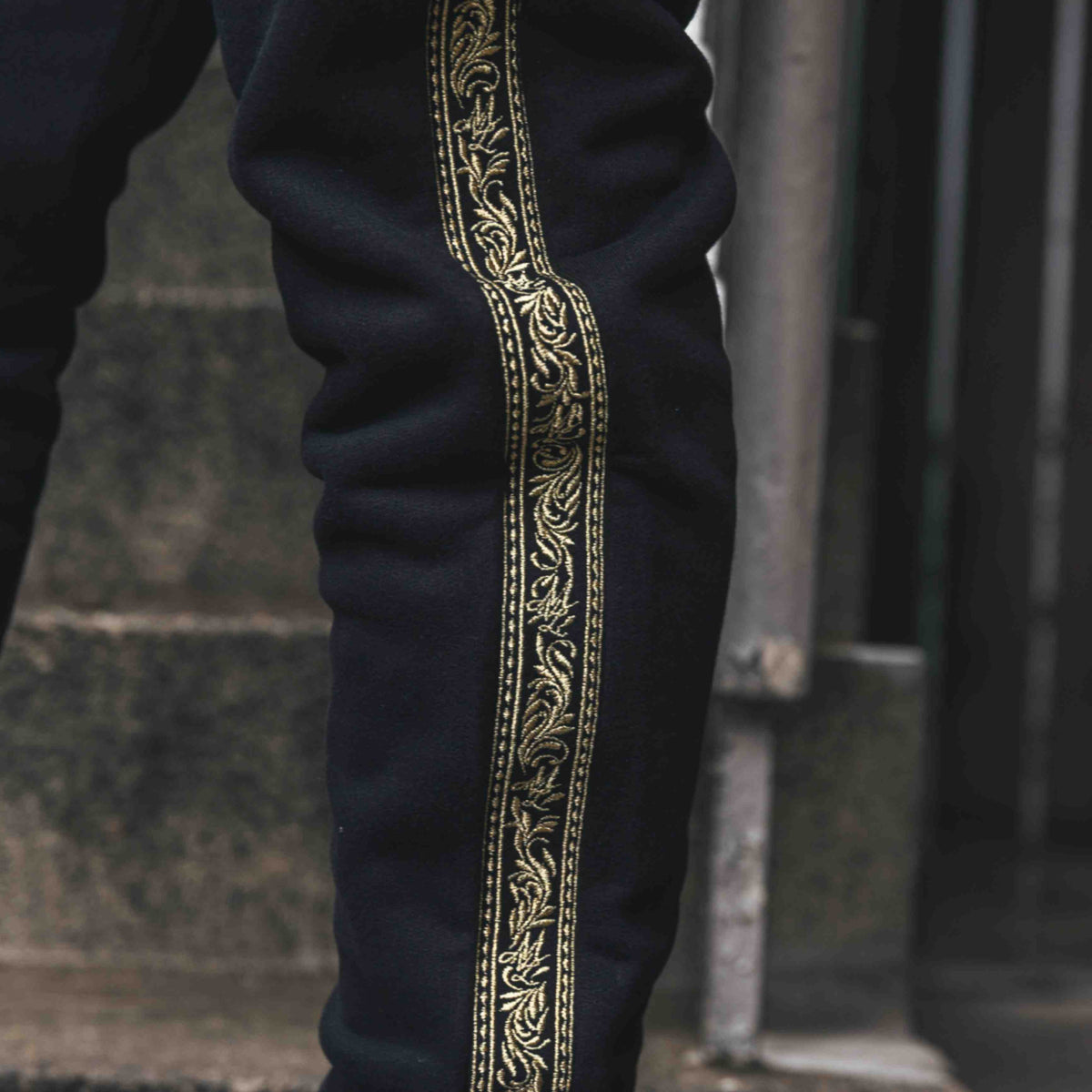 Primo piano della banda ricamata Meander dorata lungo la gamba dei pantaloni jogger MVL neri