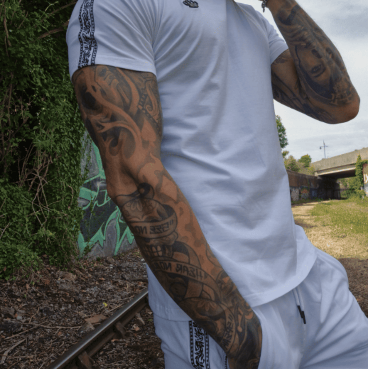 Mannequin en T-shirt MVL blanc et short Meander blanc près de rails avec graffitis