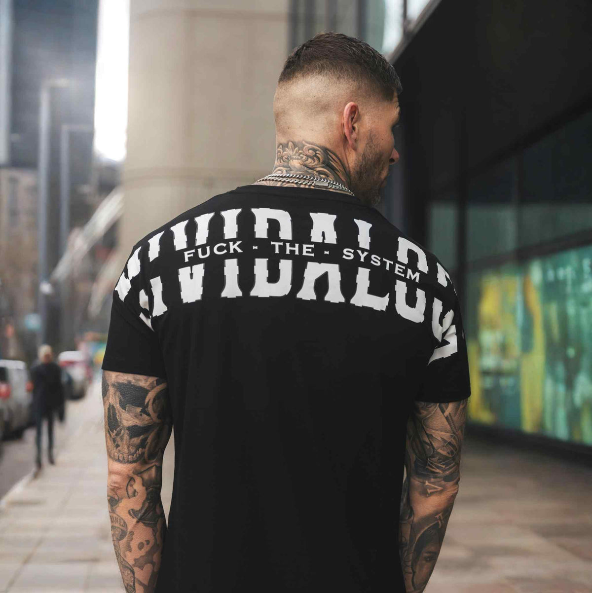 Tył czarnej koszulki FTS z białym nadrukiem Mi Vida Loca na plecach, na modelu na ulicy