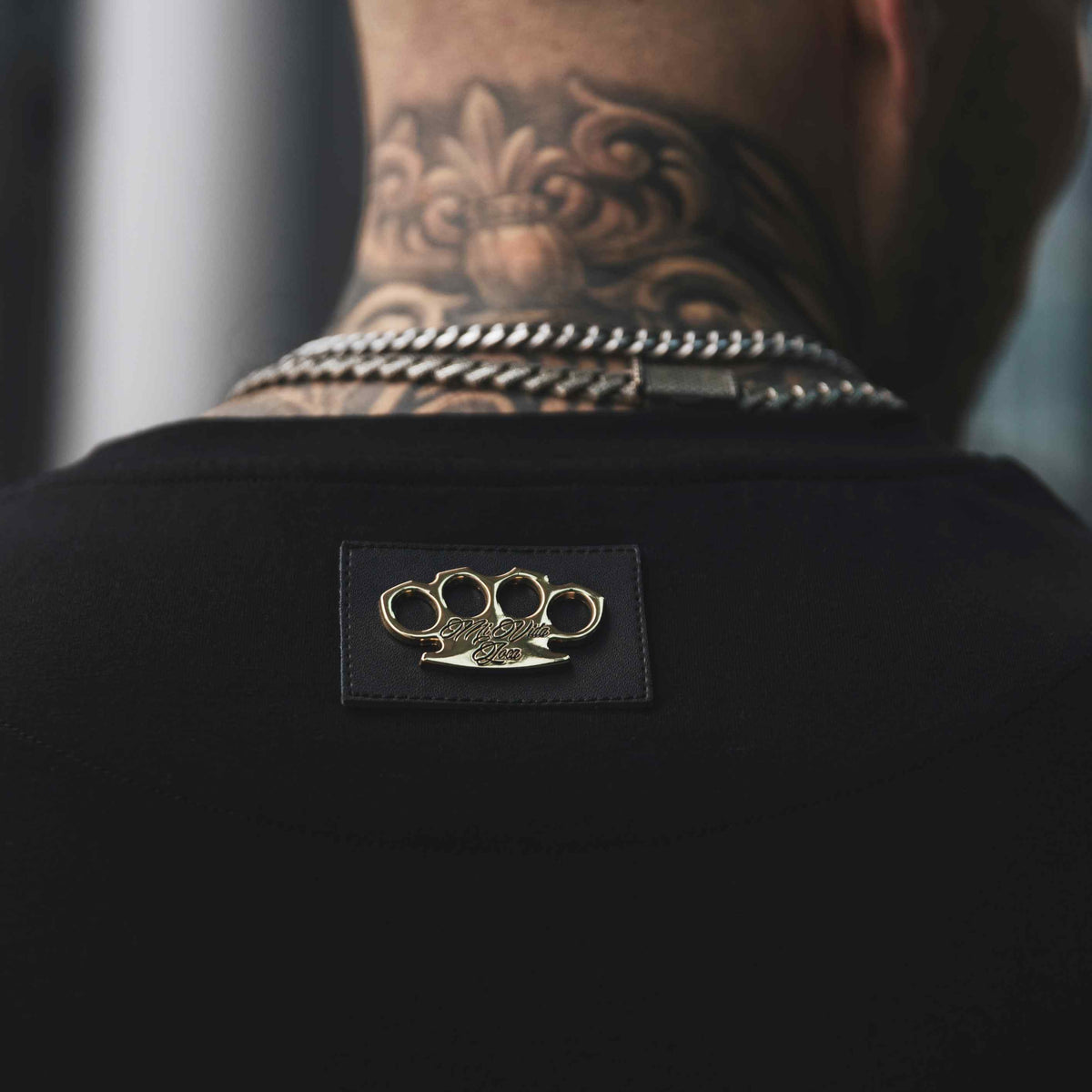 Nahaufnahme des goldenen MVL-Logos auf Patch im Nacken des schwarzen Helix T-Shirts, getragen
