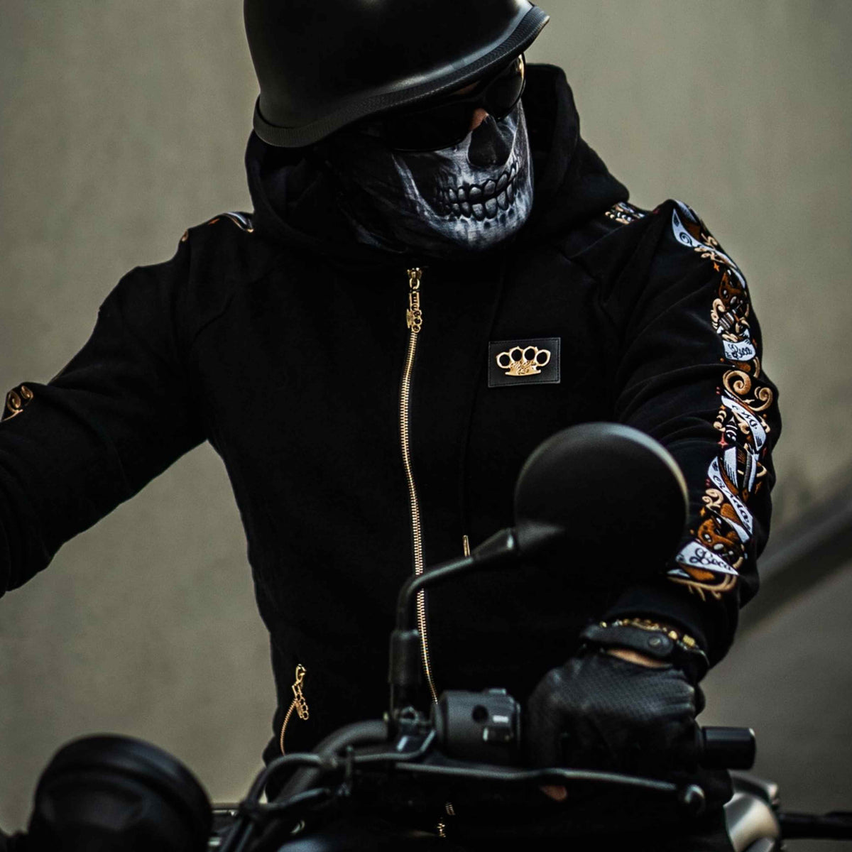 Model mit Totenkopfmaske und Helm im schwarzen Savage ornate Hoodie auf einem Motorrad