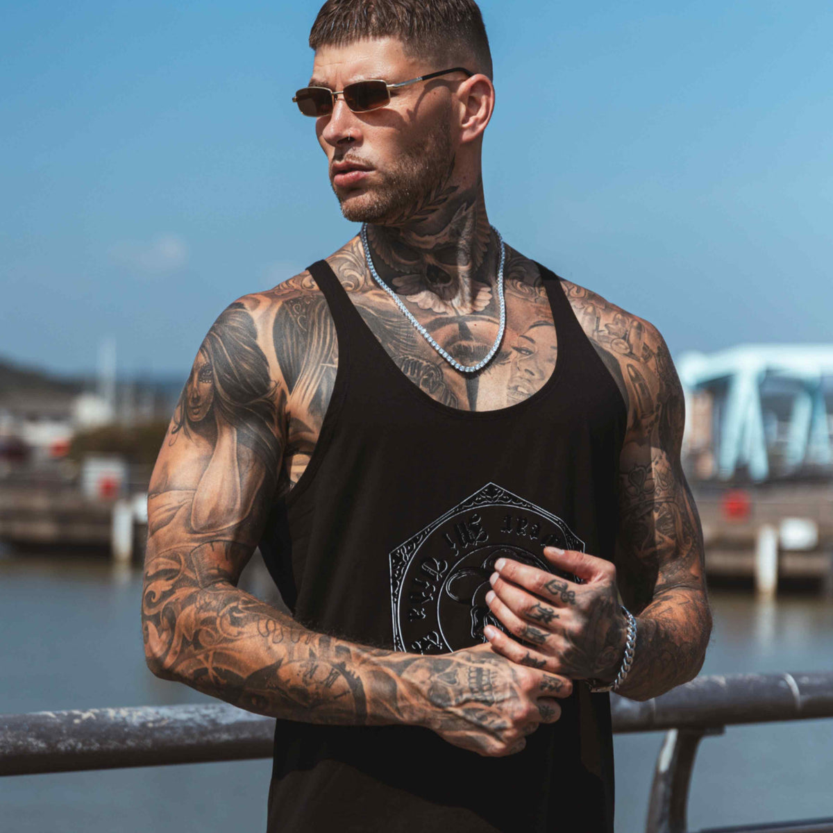 Camiseta de tirantes MVL Original streetwear negra llevada por modelo con gafas de sol y cadena plateada, delantera