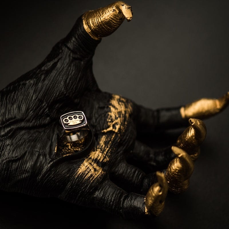 Anillo de sello MVL plateado en una escultura de mano negra y dorada, foto ambiental