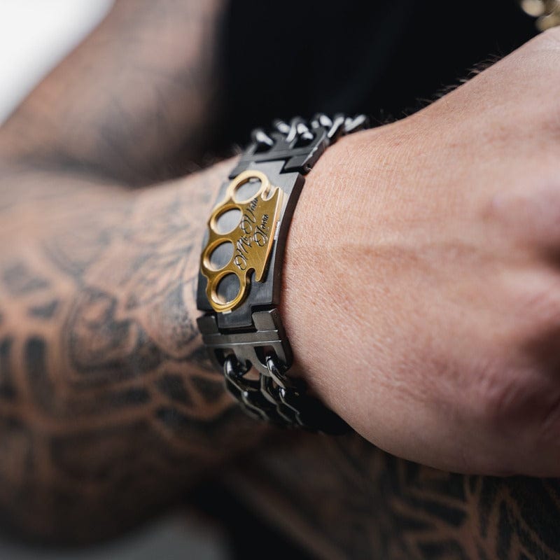 MVL Bracelet zwart/goud om de pols van een getatoeëerde arm, gouden MVL logo in beeld