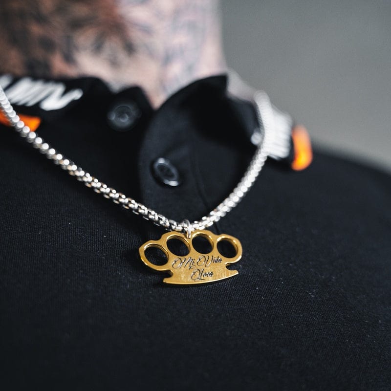 Cadena MVL Logo plata/oro llevada sobre una camiseta negra, primer plano del colgante